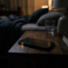 Smartphone with glowing orange notification light on wooden bedside table