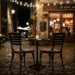 Two empty chairs and a small table with a candlelit jar outside a lit cafe at night